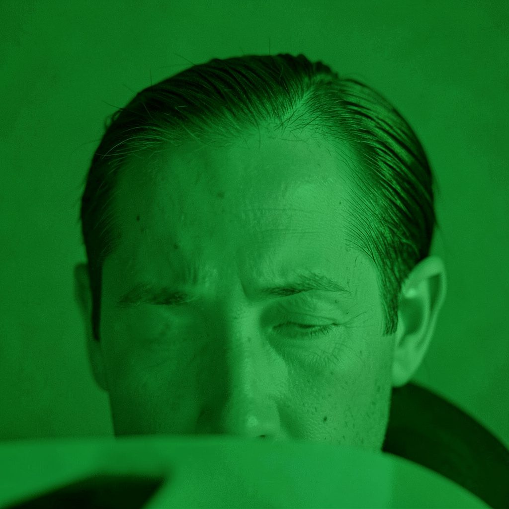 A duotone photograph of a close-up portrait showing a receding hairline against a deep teal background, conveying a thoughtful and reassuring mood